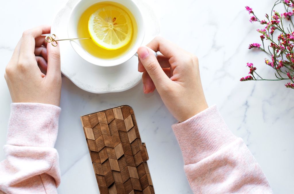 Handen met een Book Style Case voor iPhone 15 Wooden Cubes en een kopje thee met citroen.