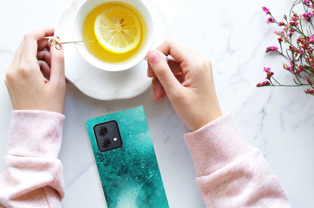Bookcase Motorola Moto G84 Painting Blue smartphone met een groene achtergrond en een kopje thee