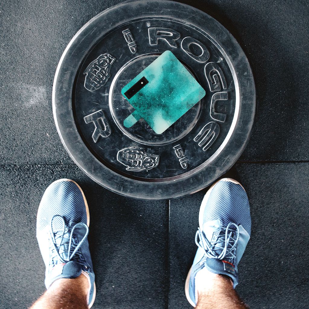 Rogue gewichtsschijf met groene dumbbell boven schoeisel op gymvloer