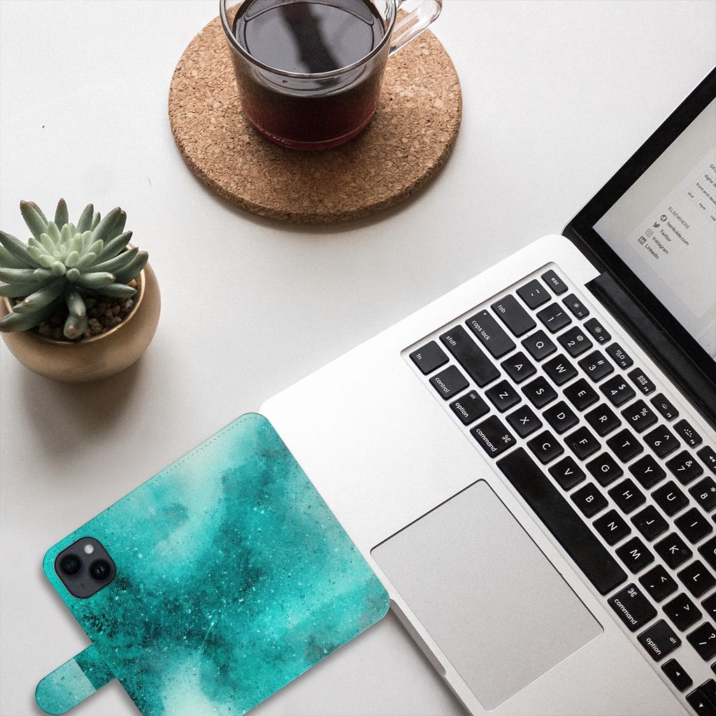 Hoesje iPhone 15 Painting Blue met prachtig blauw paletdesign, naast een laptop en een kopje koffie.