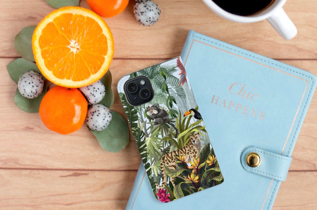 Hoesje maken voor iPhone 15 Jungle met tropisch dierenontwerp op houten tafel naast fruit en notitieboek.