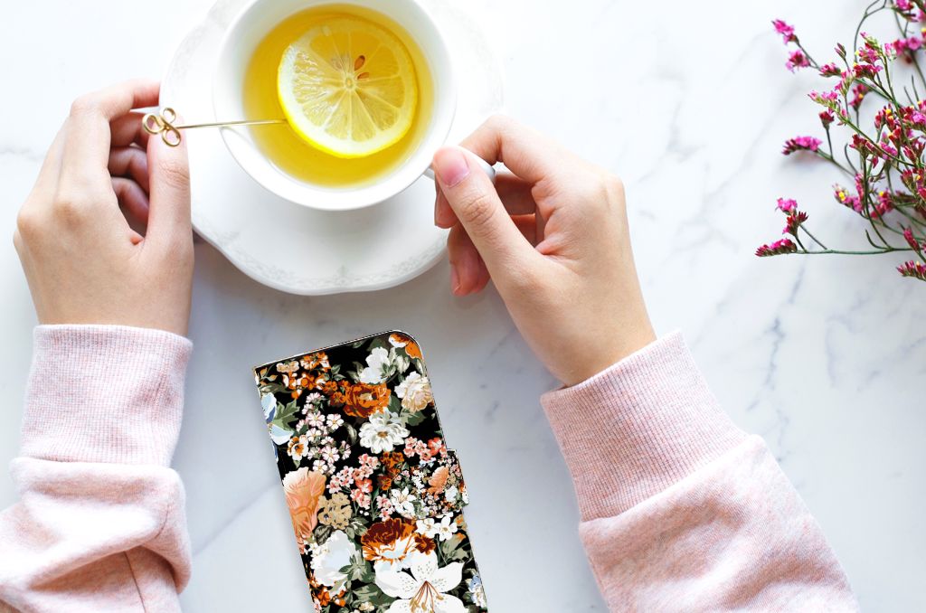 Hoesje voor iPhone 15 Dark Flowers met bloemenprint, naast een kopje thee met citroen 🍋.