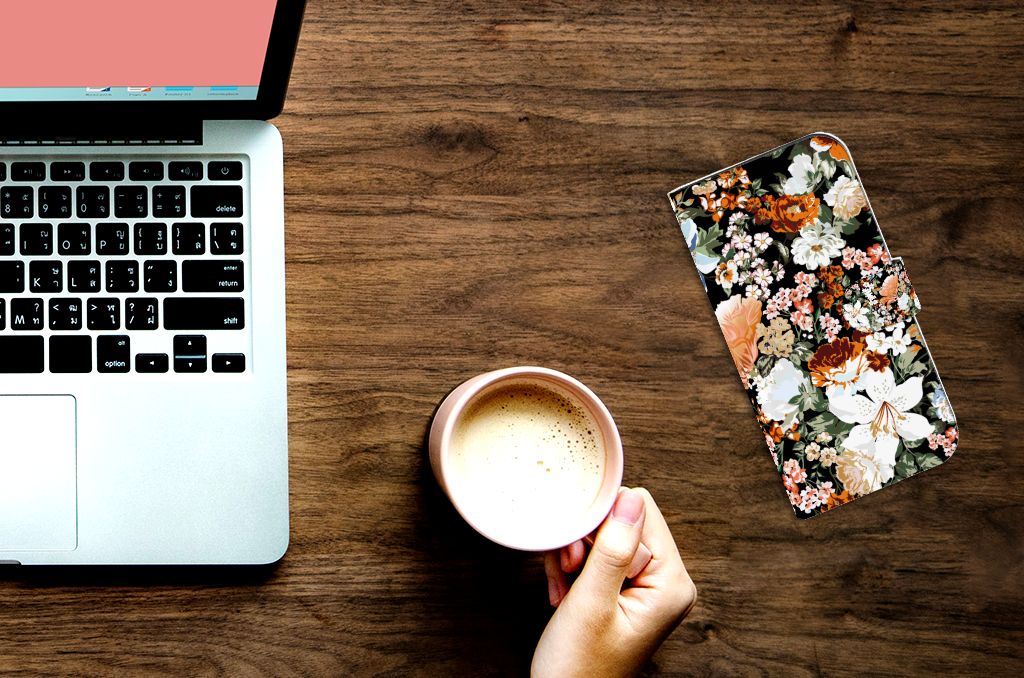 Hoesje voor iPhone 15 Pro Max Dark Flowers naast een laptop en een kop koffie op een houten tafel.