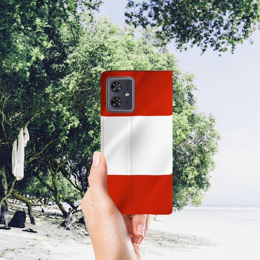 Motorola Moto G54 Standcase Oostenrijk met vlagontwerp in hand op strand, symboliseert gebruiksgemak en bescherming.