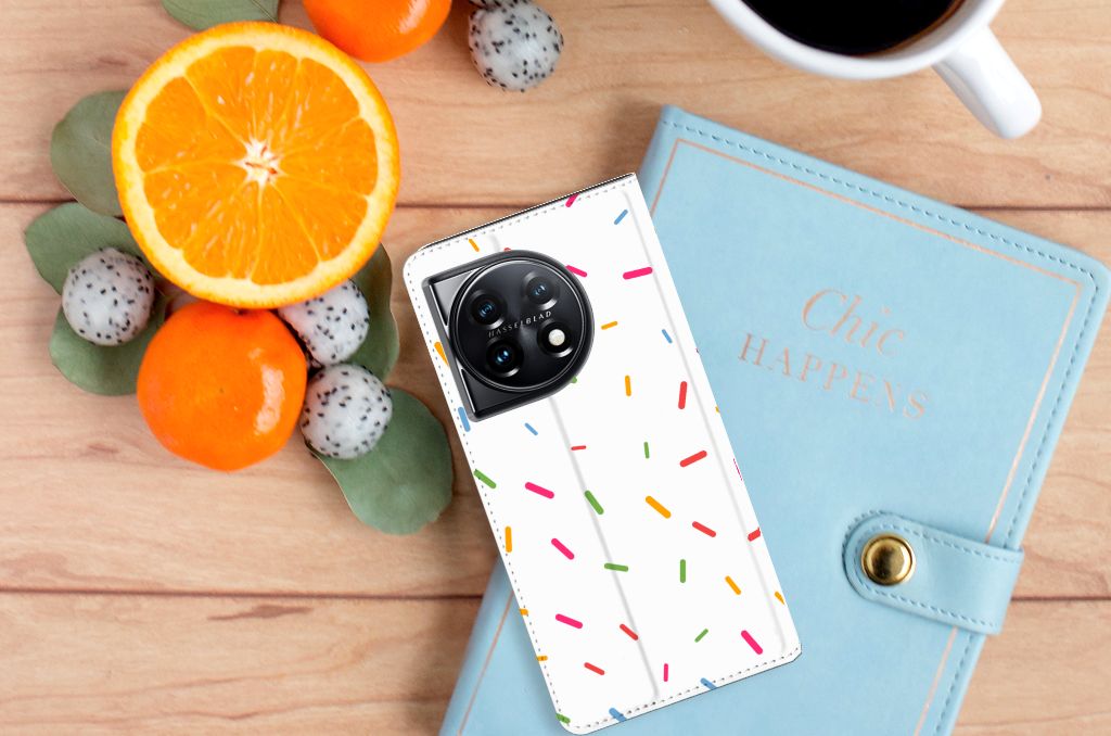 OnePlus 11 Flip Style Cover Donut Roze hoesje met sprinkles op tafel met citrusvruchten en notitieboek