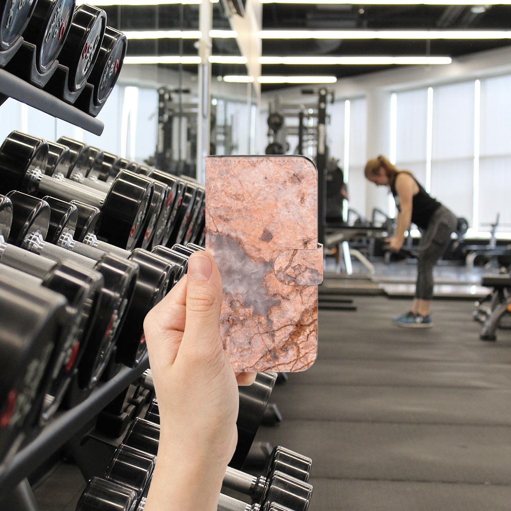 Samsung Galaxy S24 Bookcase Marmer Oranje in hand bij fitnessapparatuur voor gebruiksgemak en uitstraling.
