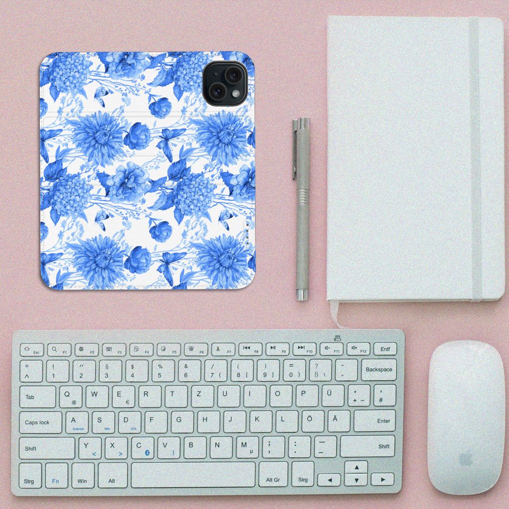 Smart Cover voor iPhone 15 Flowers Blue met blauw bloemenontwerp op een bureau met toetsenbord en notitieboekje.