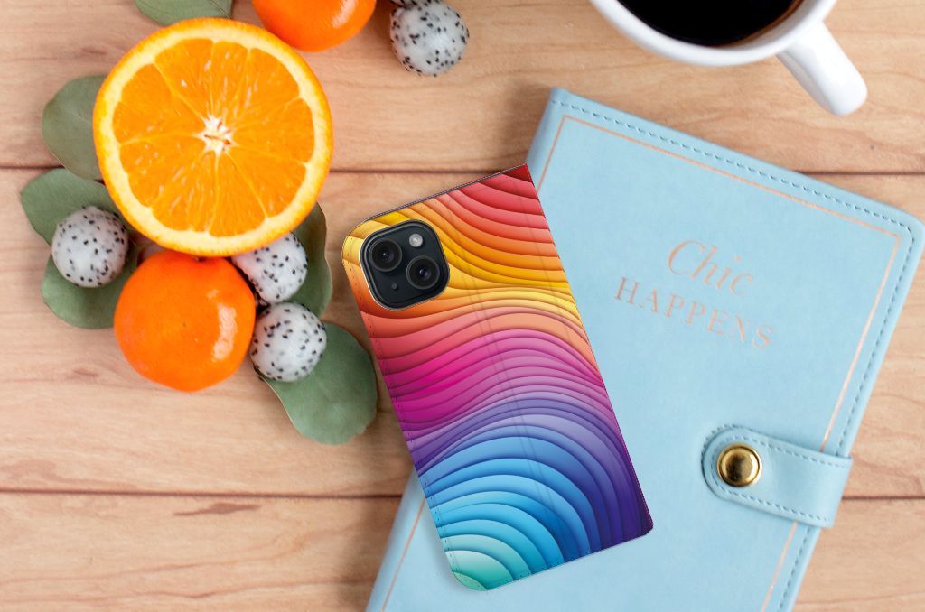 Stand Case voor iPhone 15 Regenboog met kleurrijke golven op een houten tafel met fruit 🍊.
