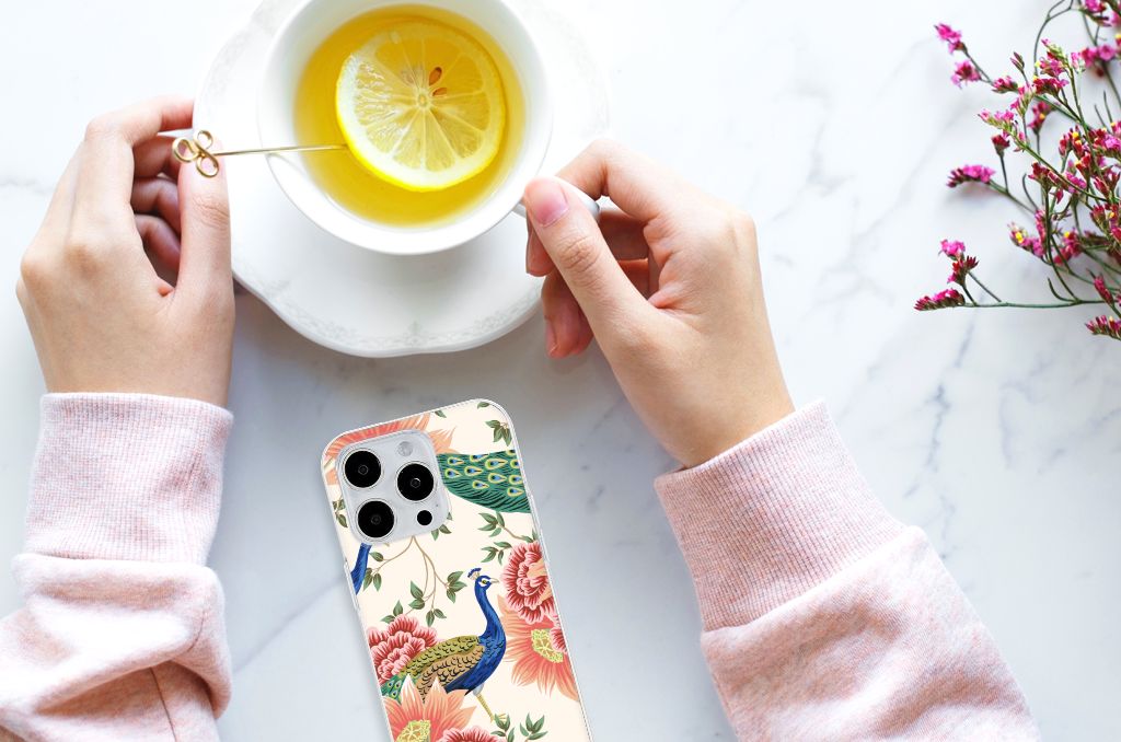 TPU Hoesje voor iPhone 15 Pro Max Pink Peacock met een paarse pauw en bloemen, in een hand met een kopje thee.