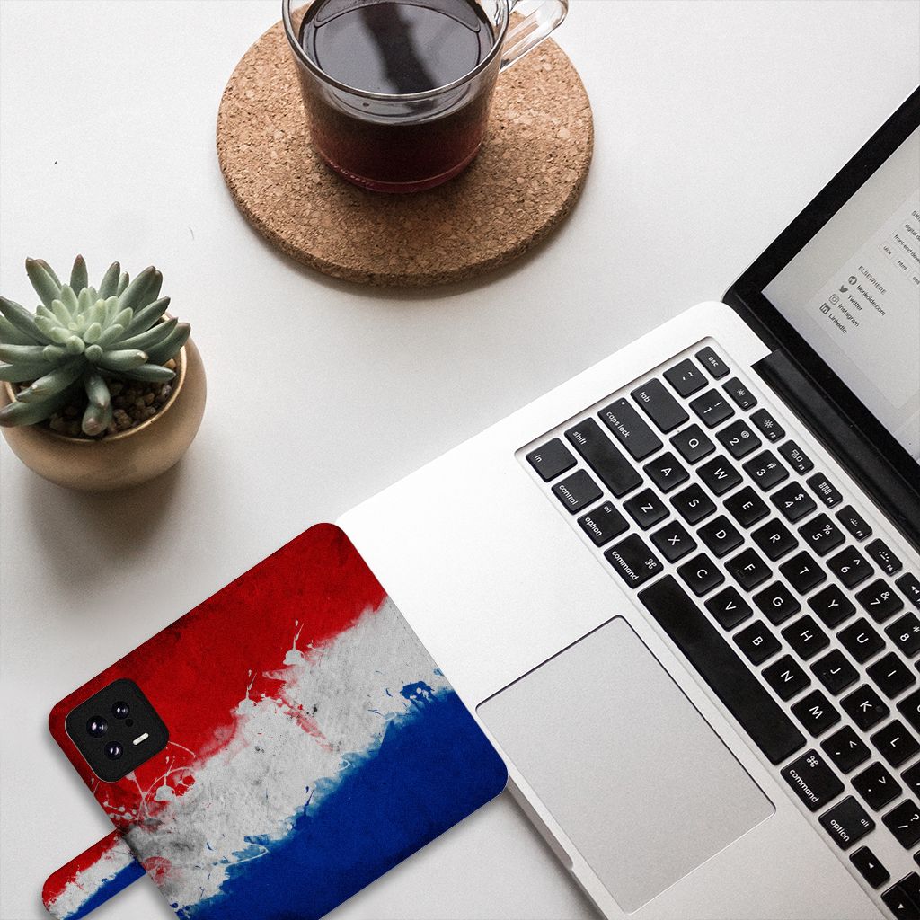 Xiaomi 13 Bookstyle Case Nederland met artistiek design van de Nederlandse vlag op een bureau met laptop en koffie.
