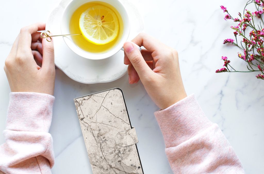 Xiaomi Redmi Note 12 4G Bookcase Marmer Beige met een lichte hand die thee drinkt, ideaal als cadeau voor stijl en bescherming.