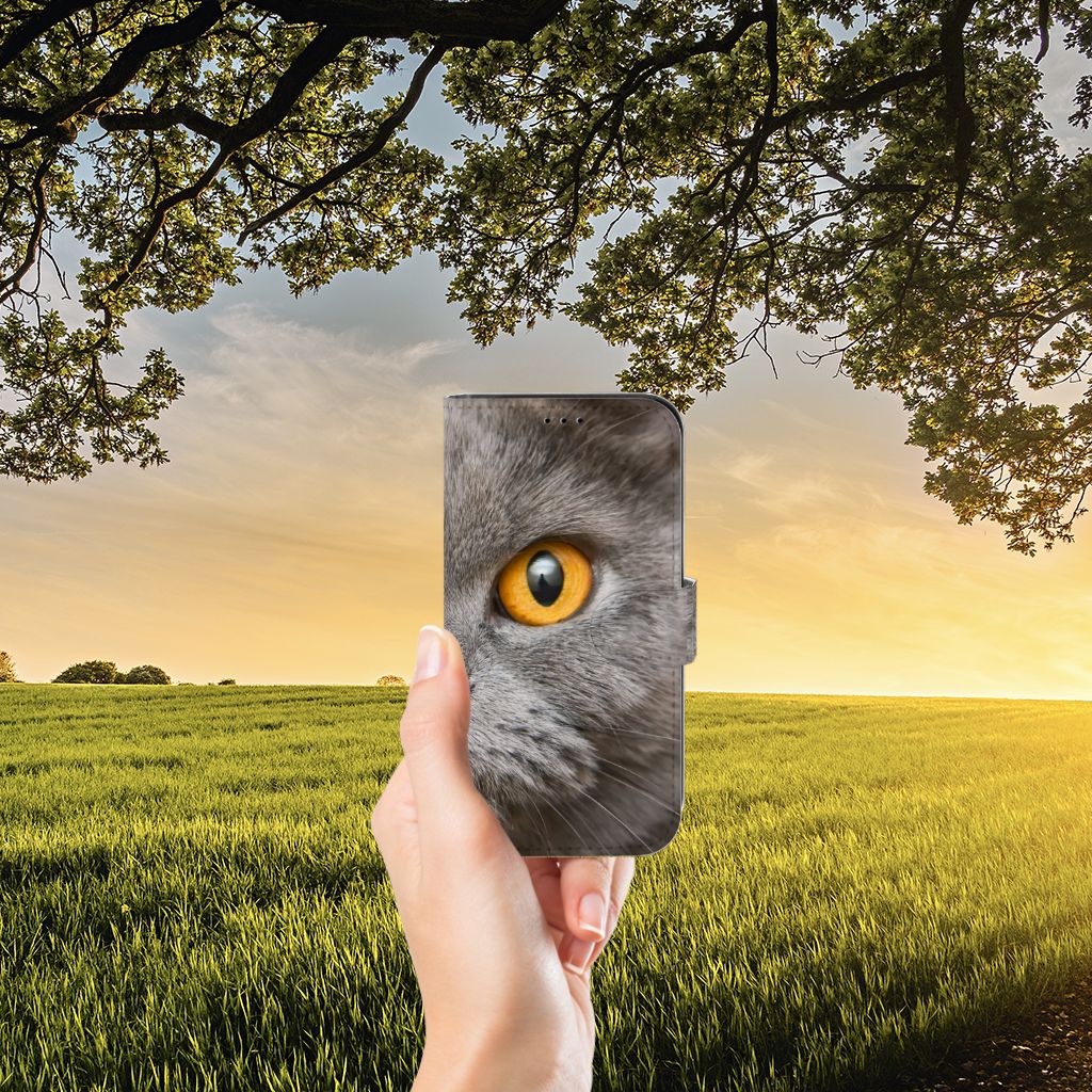 Telefoonhoesje met Pasjes Apple iPhone 13 Britse Korthaar met een grijze kat met gele ogen tegen een natuurlijke achtergrond.