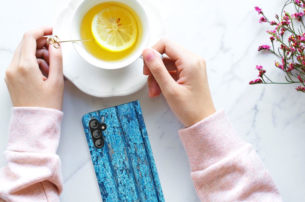 Samsung Galaxy A14 5G Book Wallet Case Wood Blue next to a cup of tea and flowers.