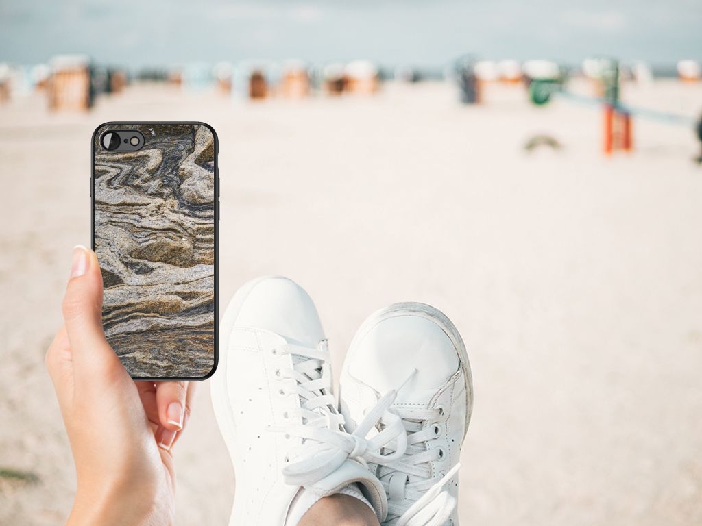 Vrouw houdt een iPhone SE 2022 | SE 2020 | 7/8 Marmeren Print Telefoonhoesje Steen vast op het strand.