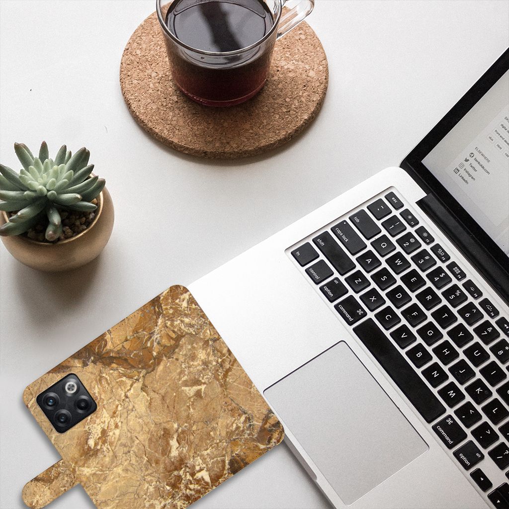 OnePlus 10T Bookcase Marmer Creme op een bureau naast een laptop en een plant.