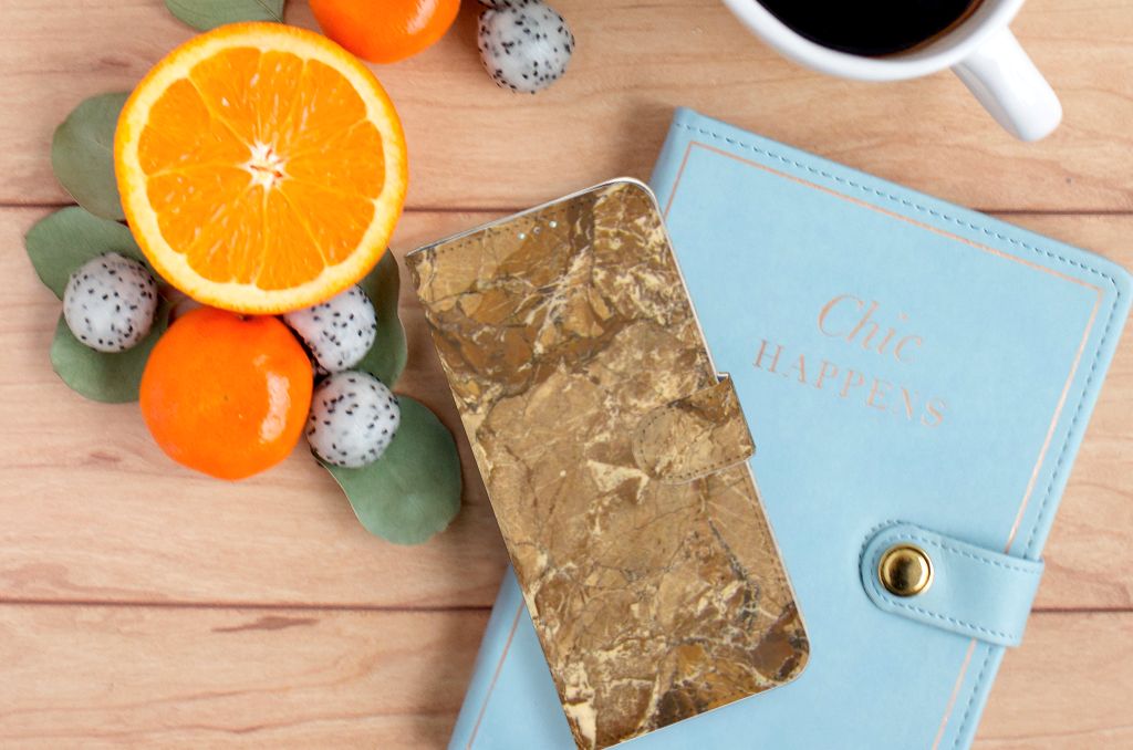 Samsung Galaxy A71 Bookcase Marmer Creme op een houten tafel met fruit en een agenda.