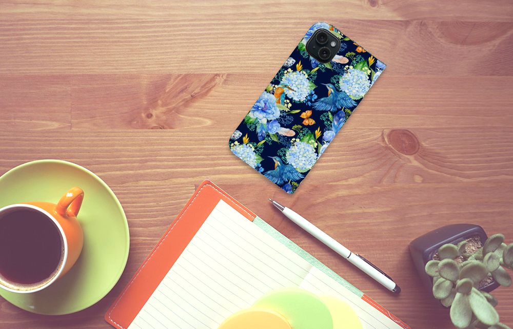 Hoesje maken voor iPhone 15 Plus IJsvogel met bloemenprint op een bureau naast een kop koffie.