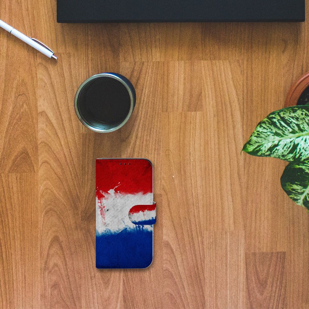 iPhone 13 Mini Bookstyle Case Nederland met artistiek ontwerp van de Nederlandse vlag op houten tafel.