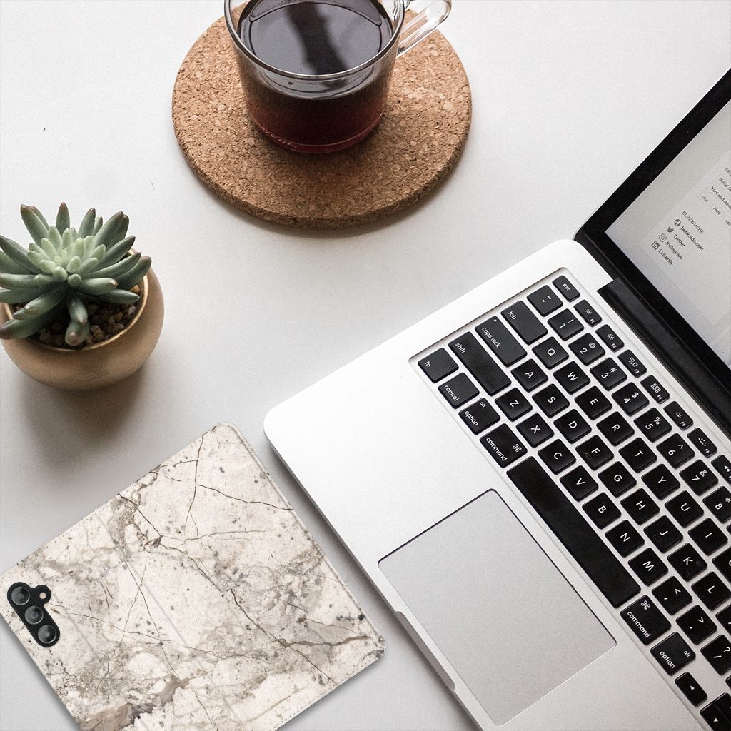 Samsung Galaxy A14 5G Standcase Marmer Beige op een bureau naast een laptop en een plant.