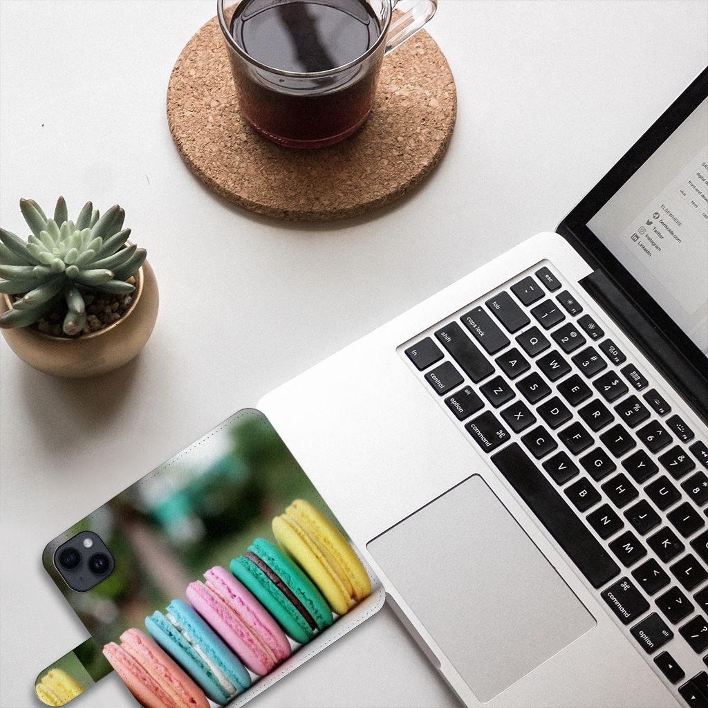 iPhone 15 Book Cover Macarons met kleurrijke macarons op een bureau naast laptop en plant 🌿.