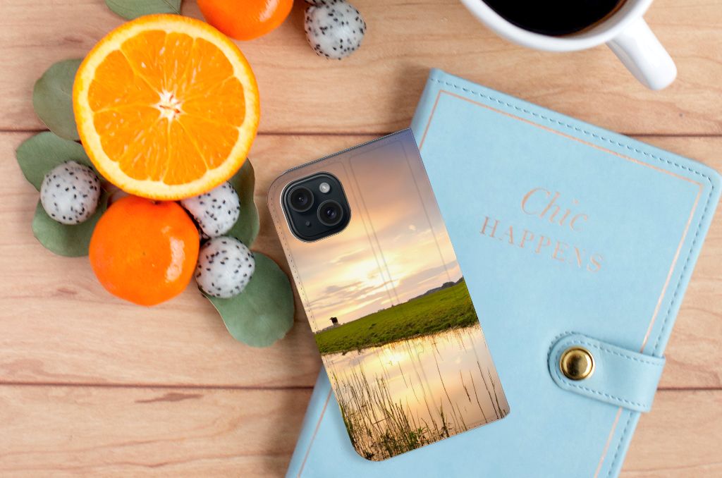 iPhone 15 Hoesje maken Koe met ondergang van de zon, stijlvolle case op een bureau met citrusvruchten.