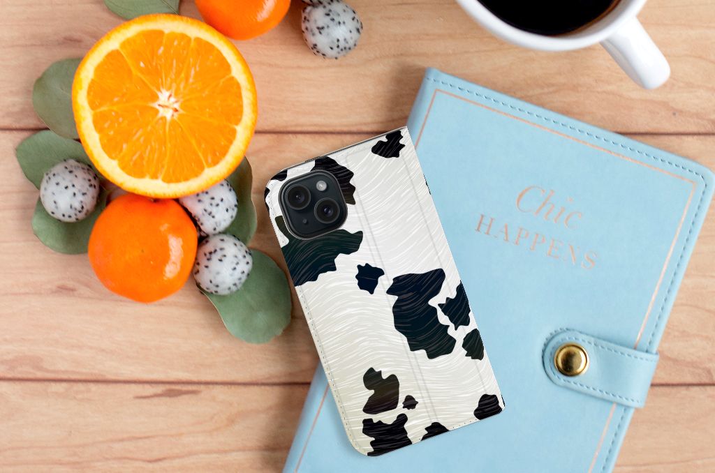 iPhone 15 Hoesje maken Koeienvlekken met een stijlvolle, hoogwaardige print op een tafel met fruit en een notitieboekje.