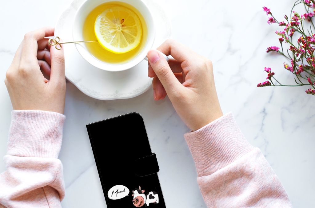 Vrouwelijke handen met een iPhone 15 Leuk Hoesje Cow en een kom met citroenthee op een marmeren tafel.