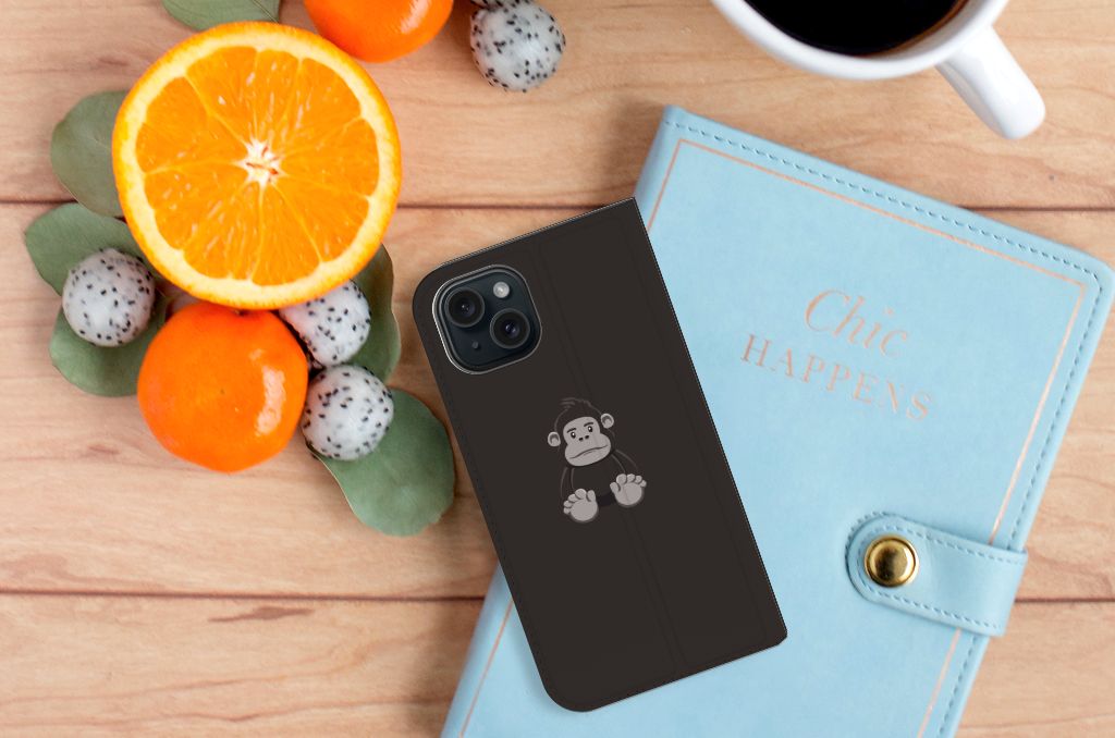 iPhone 15 Magnet Case Gorilla met schattig aapjesdesign📱, gezet op een houten tafel met fruit en een notitieboek.