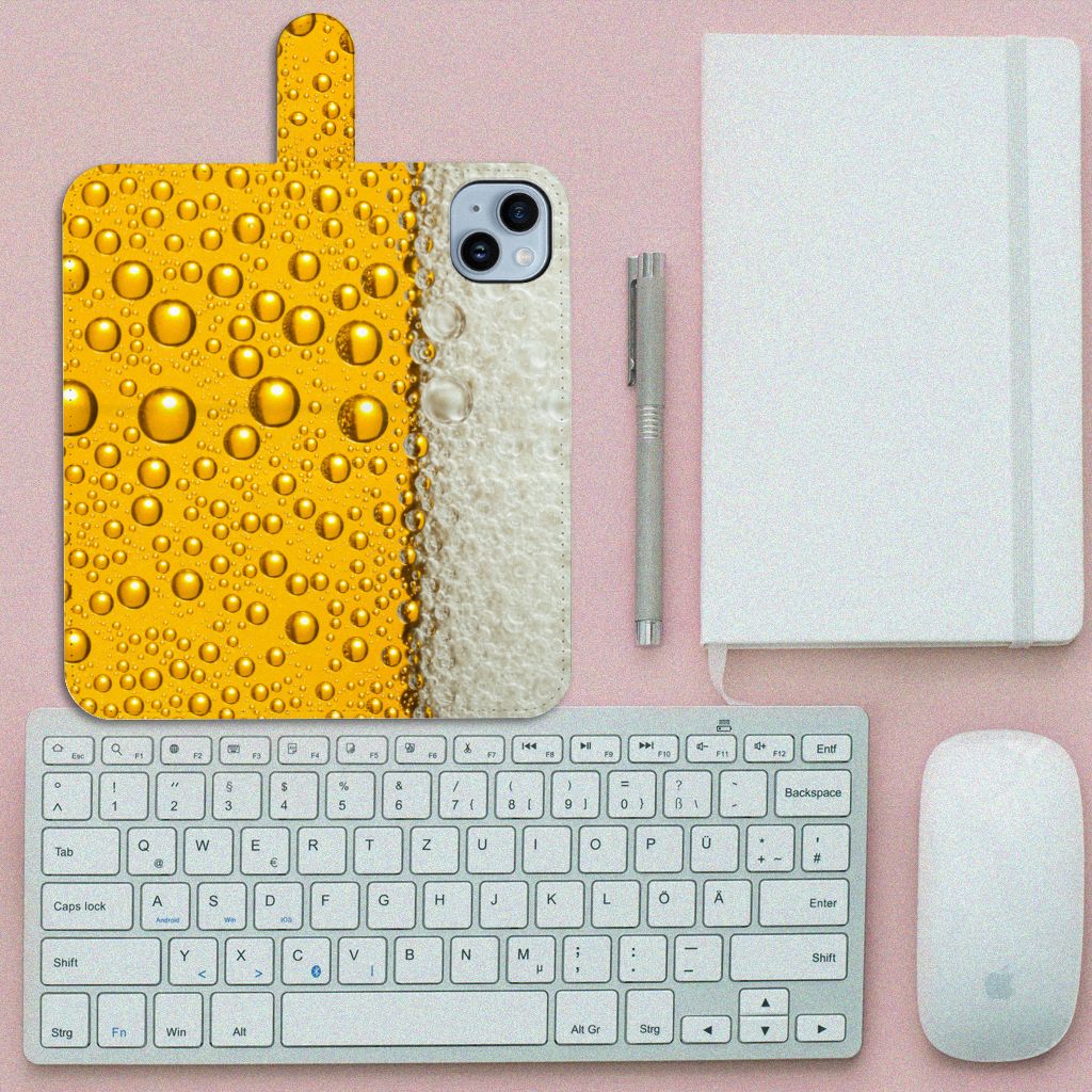 iPhone 15 Plus Book Cover Bier met biertjes en druppels op een bureau naast een toetsenbord en notitieboek