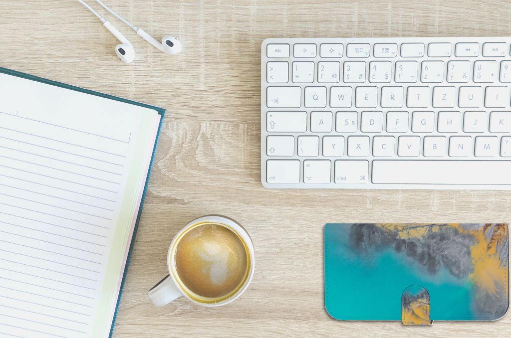 iPhone 15 Plus Bookcase Marble Blue Gold met een koffie en notitieboek op een bureau.