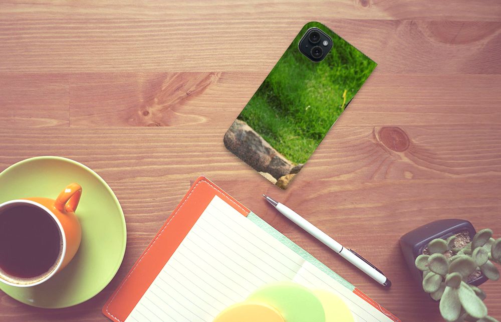 iPhone 15 Plus Hoesje maken Panda met groen gras achtergrond op een bureau met een kopje koffie en notitieboek.