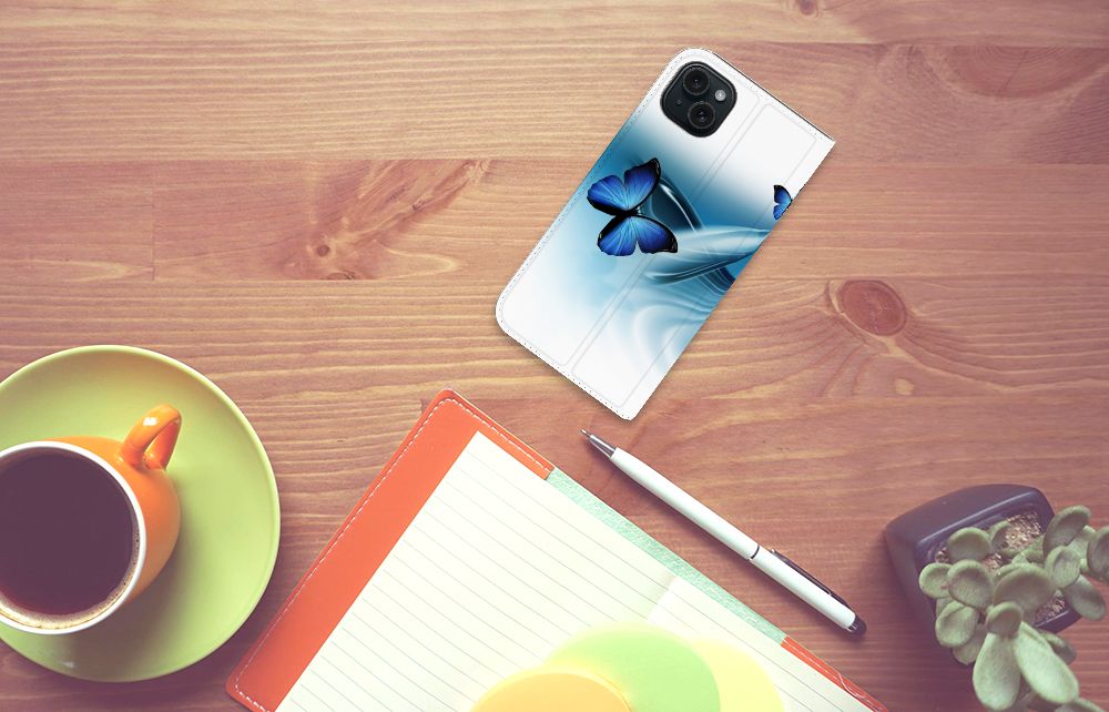 iPhone 15 Plus Hoesje maken Vlinders met blauwe vlinders op een houten tafel met koffie en notitieboek.