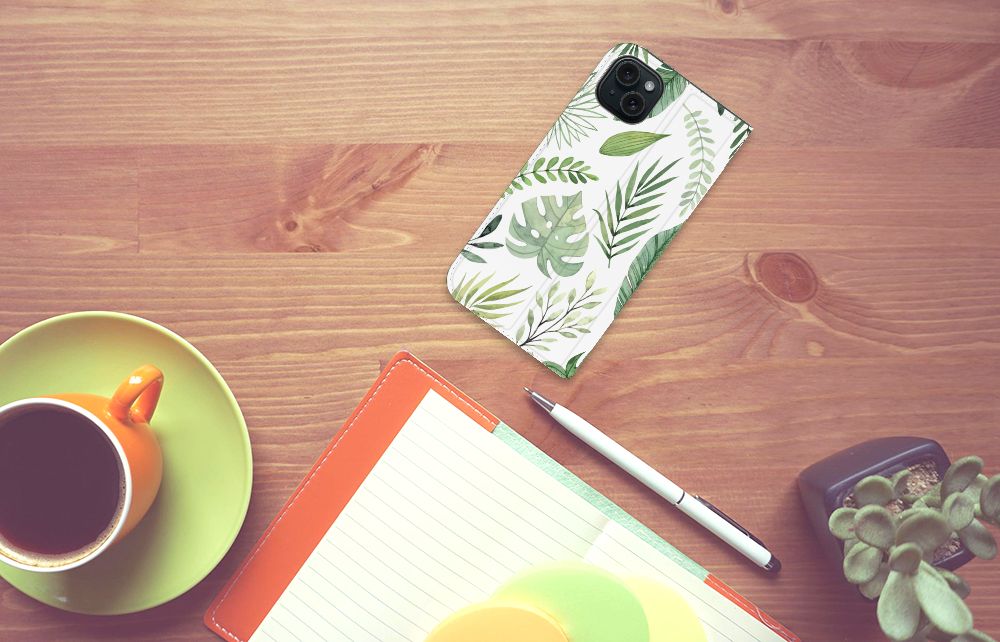 iPhone 15 Plus Smart Cover Leaves met groen bladerenprint op een bureau met een kopje koffie en notitieboek.