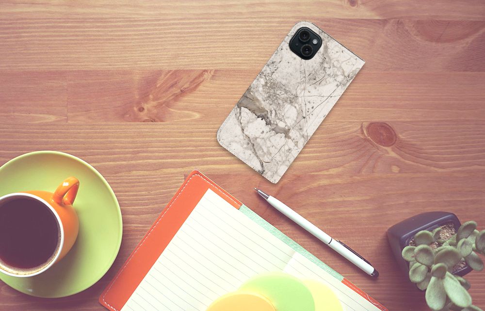 iPhone 15 Plus Standcase Marmer Beige op een houten tafel met koffie en notitieboek.