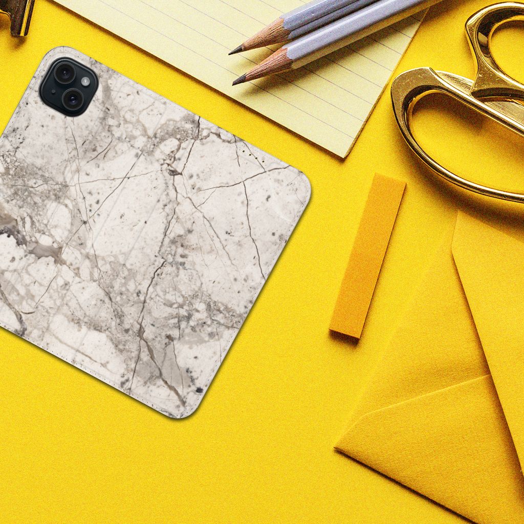 iPhone 15 Plus Standcase Marmer Beige op een gele achtergrond met pennen en scharen.