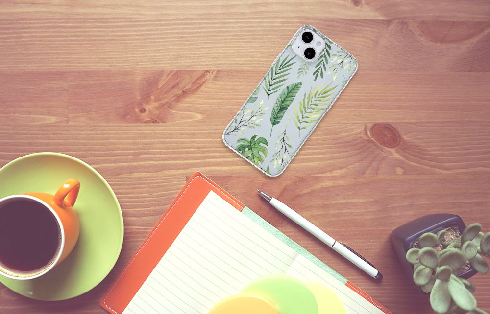iPhone 15 Plus TPU Case Leaves met groene bladeren op een houten tafel, omringd door een mok en notitieboek.