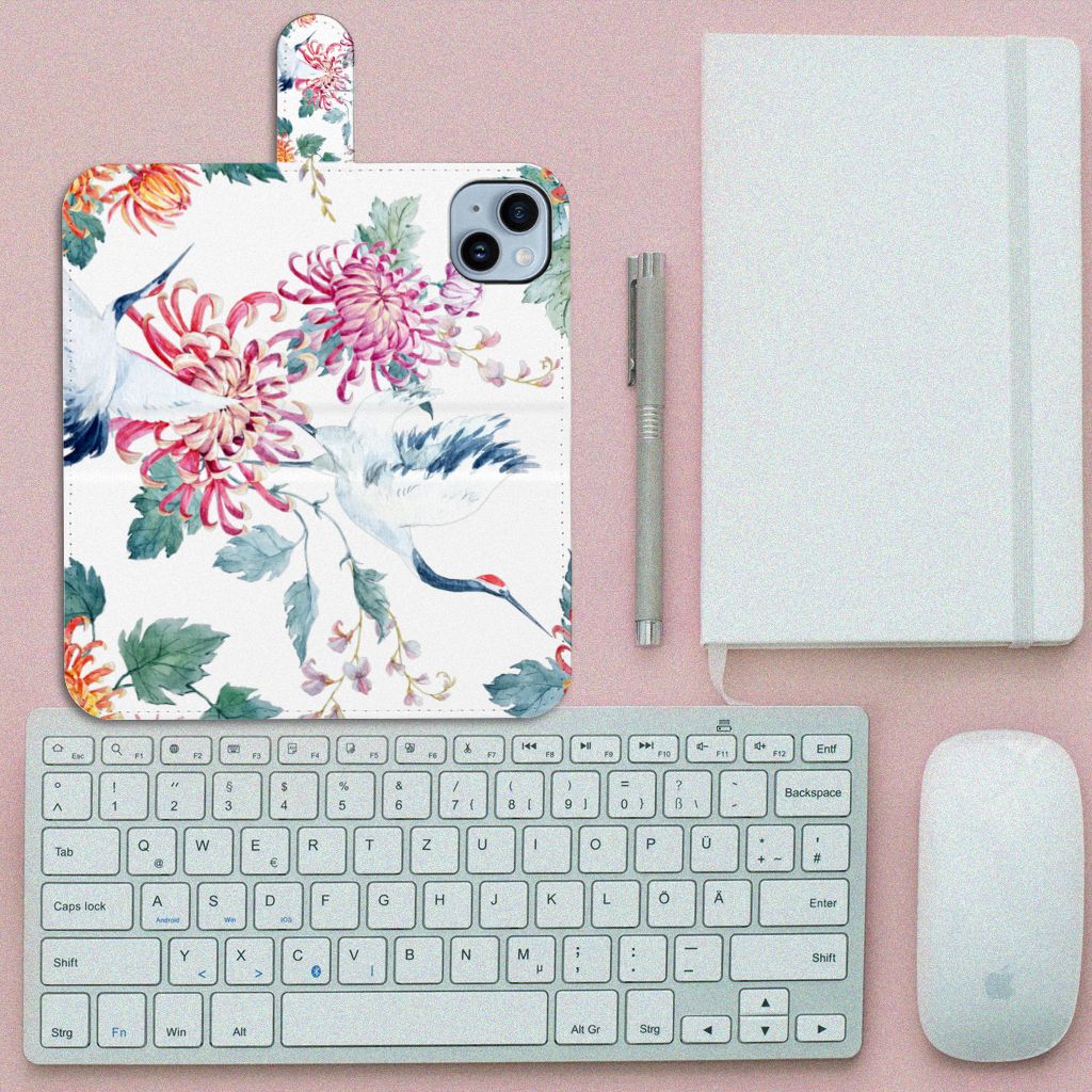 iPhone 15 Plus Telefoonhoesje met Pasjes Bird Flowers met bloemen en ooievaars op een bureau met toetsenbord en notitieboek.