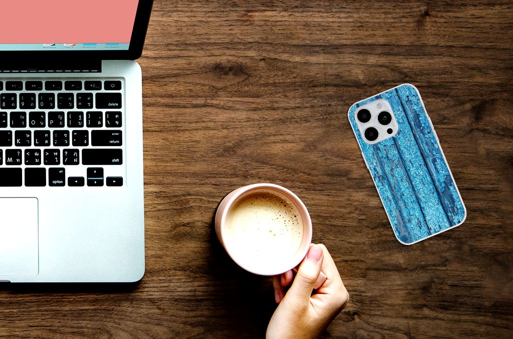 iPhone 15 Pro Bumper Hoesje Wood Blue op tafel naast laptop en koffie, met afgebladderd blauw hout design.