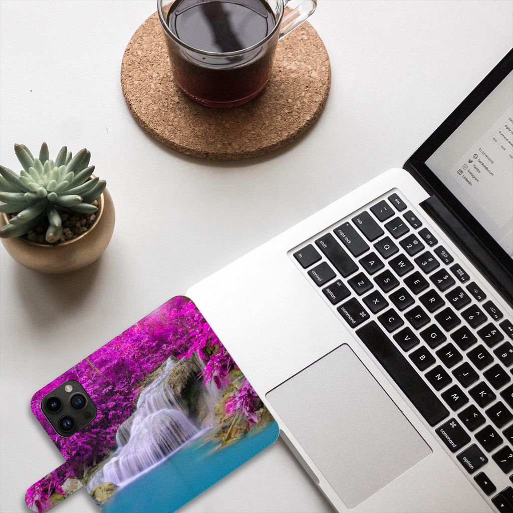 iPhone 15 Pro Flip Cover Waterval met een waterval en paarse bomen, geplaatst op een bureau met een laptop en koffie.