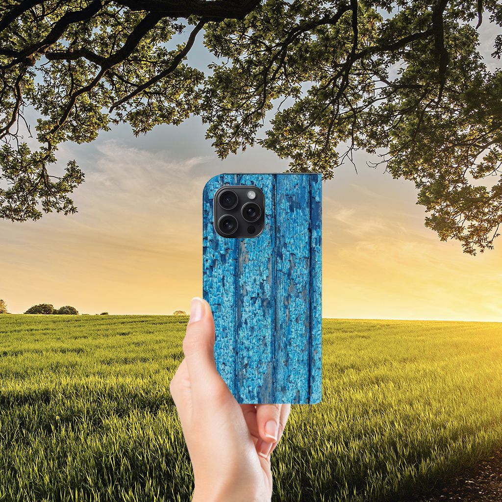iPhone 15 Pro Max Book Wallet Case Wood Blue met blauw houten design, vastgehouden tegen een zonnige achtergrond.