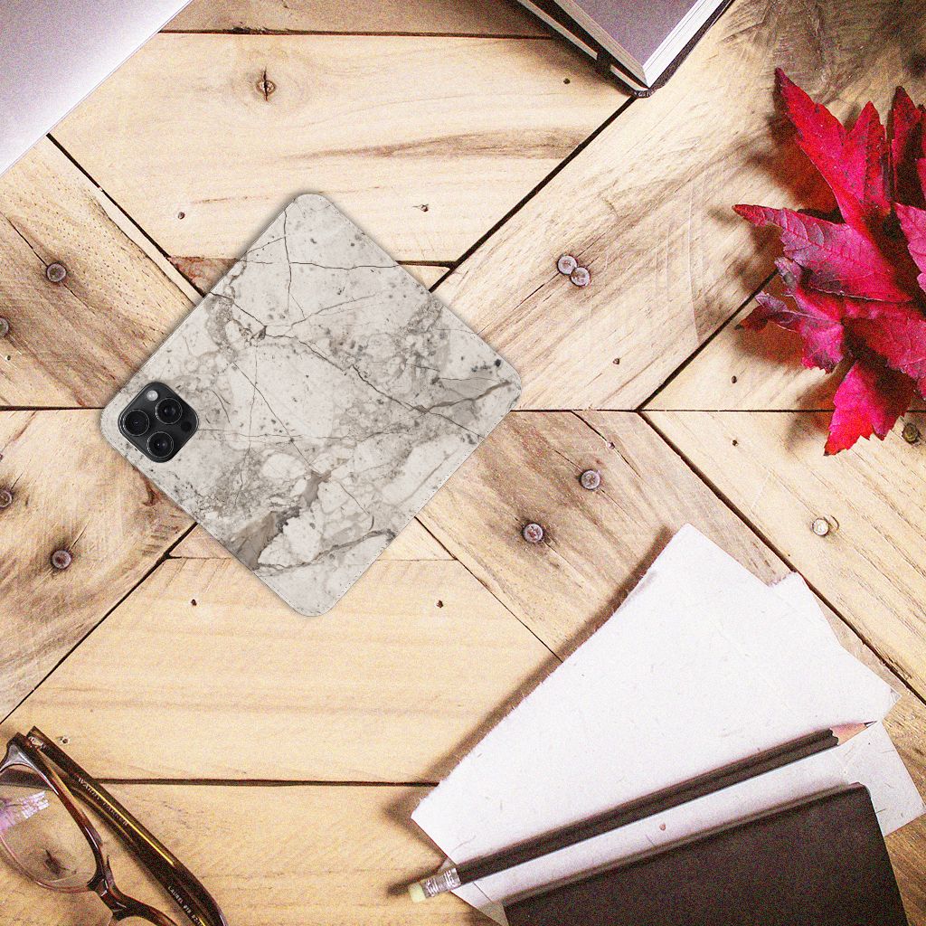 iPhone 15 Pro Max Standcase Marmer Beige op een houten tafel met een paar notities en een bril.