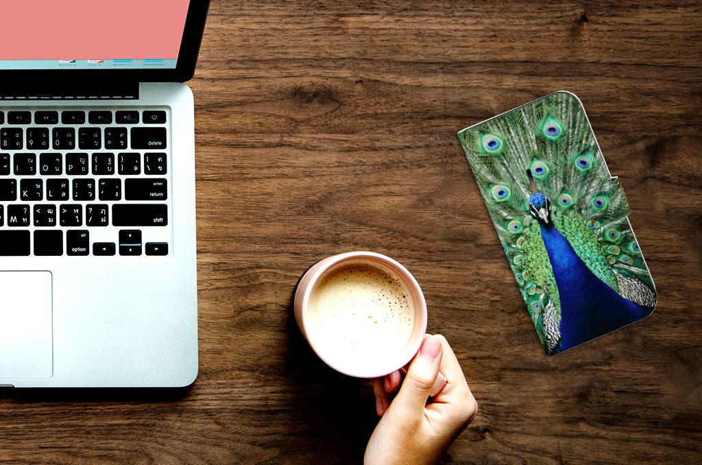 iPhone 15 Pro Max Telefoonhoesje met Pasjes Pauw voor een laptop en koffie op een houten tafel.