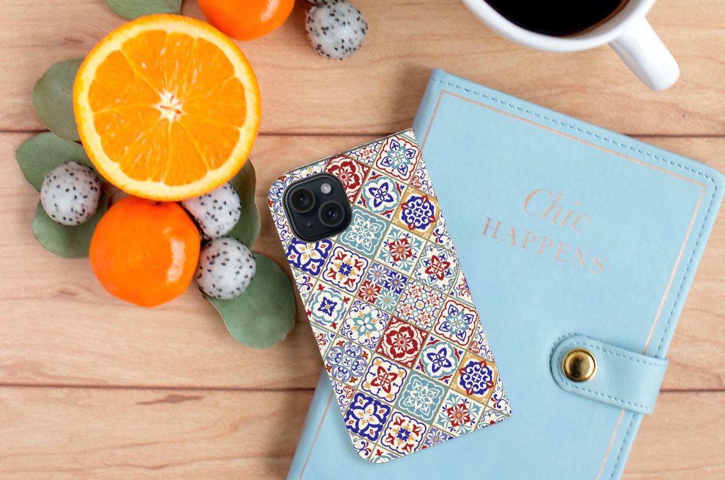 iPhone 15 Standcase Tiles Color met kleurrijk mozaïek design op een houten tafel met fruit en een notitieboekje